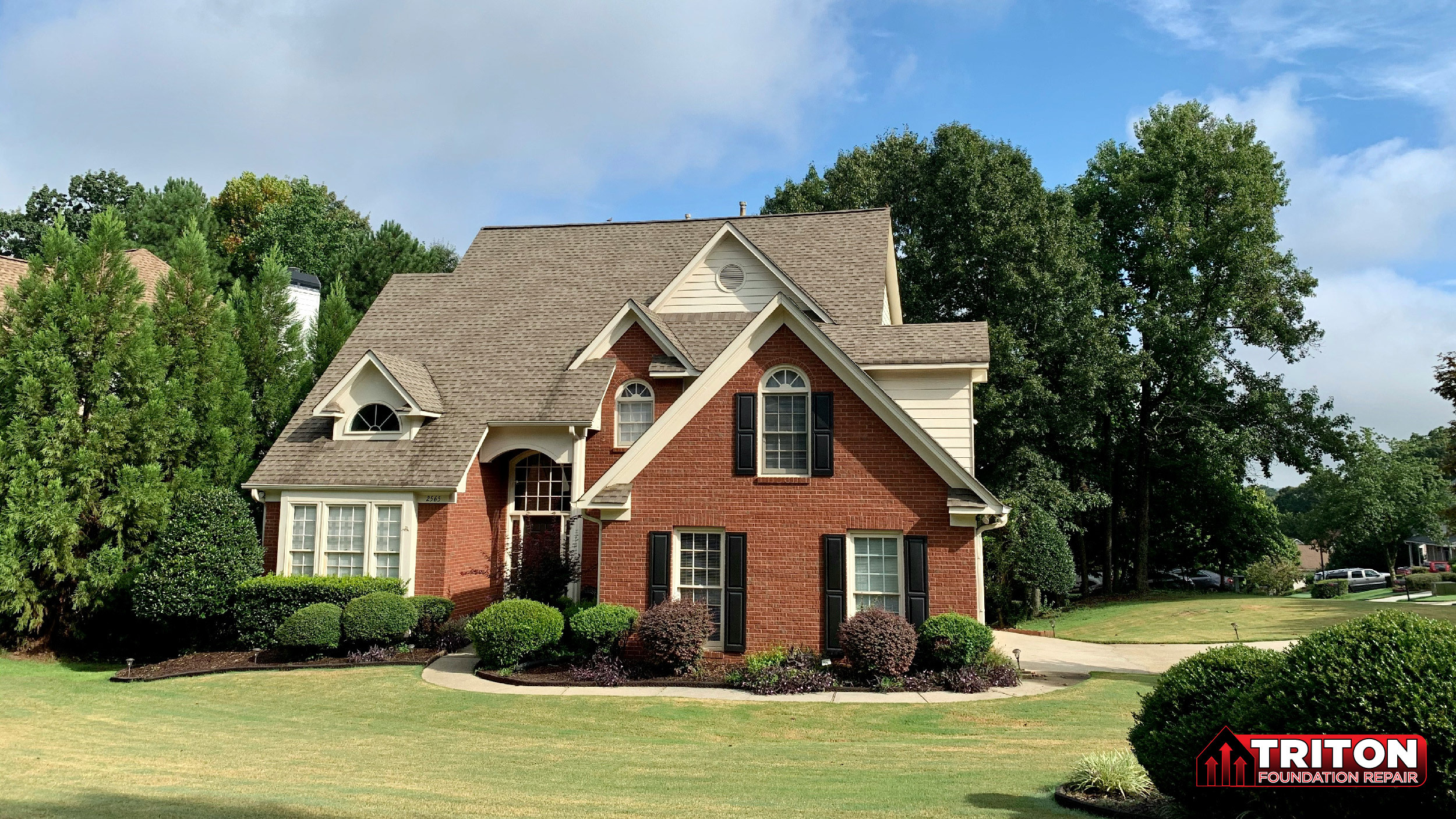 A well-maintained suburban brick two-story house with a manicured lawn and lush green landscaping